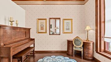 A room with a wooden piano, a patterned rug, a mirror, and a dresser with a lamp.