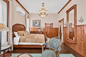 Un dormitorio con una cama de madera, un candelabro, un espejo y un amplio ventanal con cortinas.
