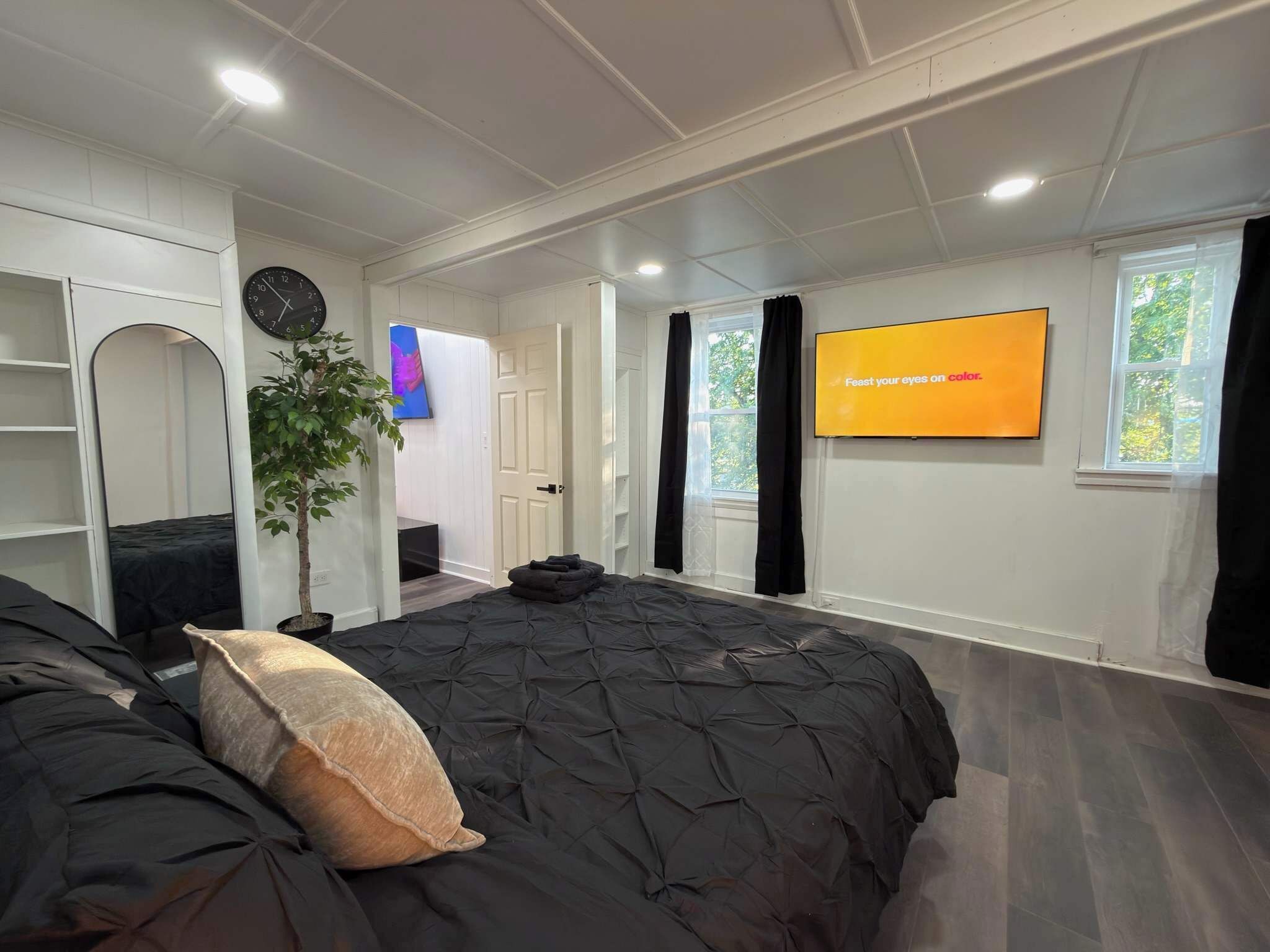 Un dormitorio con una cama, un televisor, una planta y un reloj en la pared.