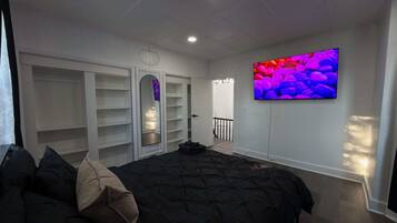 A bedroom with a bed, a wardrobe, a TV, and a door leading to another room.
