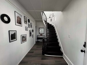 A hallway with a black spiral staircase, framed pictures on the walls, and a mirror.