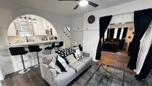 A modern living room with a sofa, a glass coffee table, and a kitchen area with bar stools.