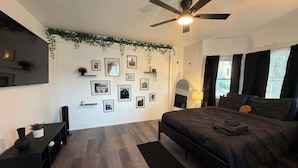 A bedroom with a bed, a ceiling fan, a wall-mounted TV, and framed pictures.