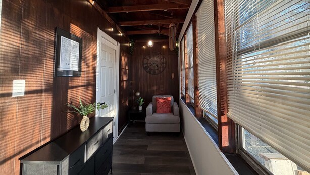 A hallway with wooden walls, a clock, a sofa, and a window with blinds.