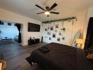 A bedroom with a bed, a ceiling fan, a TV, a console table, and a wall decorated with framed pictures.