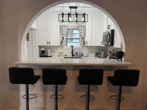 A kitchen with a central island, bar stools, a microwave, and a hanging light fixture.