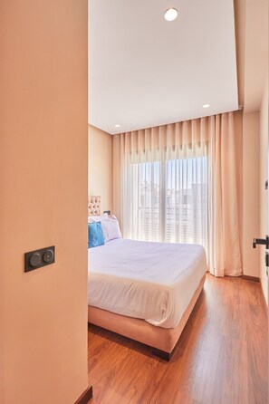 Et moderne hotelværelse med en stor seng, en sengegavl, et vindue med gardiner og en trægulv.