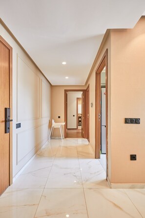 A hallway with a white chair, wooden doors, and a tiled floor. - Casablanca 2BR | Free Parking Near Maarif (Casablanca)