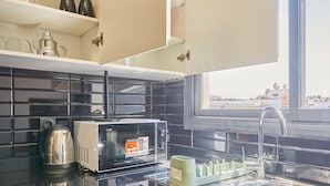 Una cocina con microondas, hervidor y una ventana sobre el fregadero.