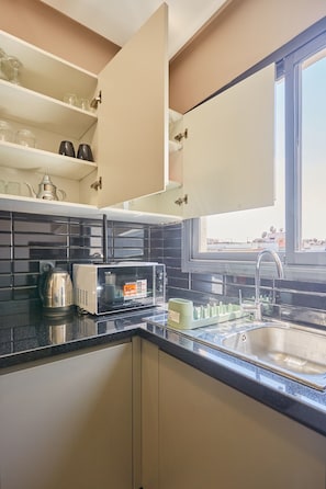 A kitchen with a microwave, kettle, and a window above the sink. - Casablanca 2BR | Free Parking Near Maarif (Casablanca)
