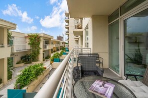 Un balcon aménagé avec du mobilier d’extérieur, une porte vitrée et une vue sur les bâtiments voisins.