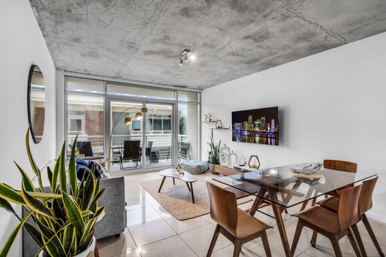 A modern dining area with a glass table, wooden chairs, and a cityscape view.