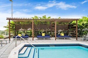 A pool area with a wooden pergola, lounge chairs, and a clear blue pool. - Modern Midtown Loft | Pool, Gym & Walk Everywhere (Miami)