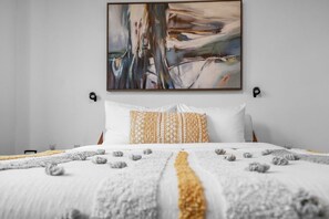 A bedroom with a bed, pillows, a blanket, and a wall-mounted abstract painting. - Modern Midtown Loft | Pool, Gym & Walk Everywhere (Miami)