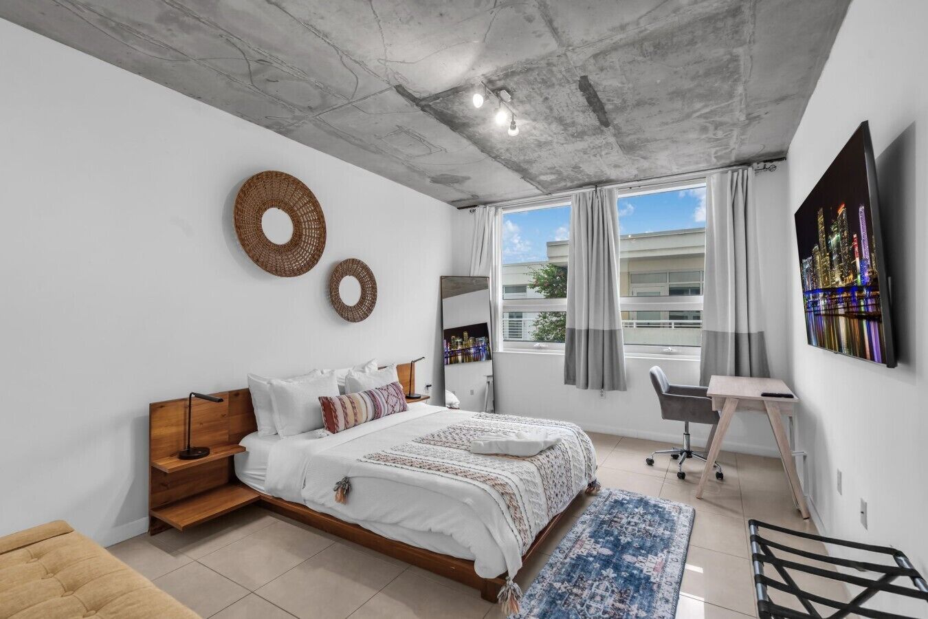 A modern bedroom with a bed, a desk, and a large window with curtains.