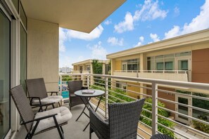 A balcony with wicker furniture, a small round table, and a view of neighboring buildings. - Modern Midtown Loft | Pool, Gym & Walk Everywhere (Miami)