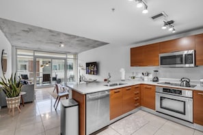 A modern kitchen with a central island, stainless steel appliances, and wooden cabinets. - Modern Midtown Loft | Pool, Gym & Walk Everywhere (Miami)