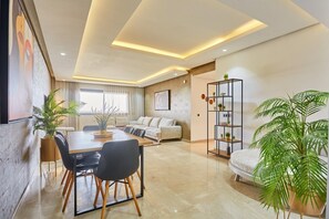 A modern living room with a sofa, a dining table with chairs, and a bookshelf. - Luxury 3BR | Prime Casablanca | Designer Stay (Casablanca)