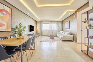 Een moderne woonkamer met een eethoek, een zithoek, een salontafel en een aan de muur bevestigde televisie.