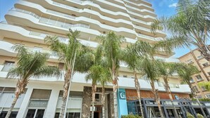 A multi-story hotel with balconies, palm trees, and storefronts including a sandwich shop. - Luxury 3BR | Prime Casablanca | Designer Stay (Casablanca)