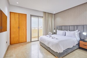 Een moderne hotelkamer met een groot bed, een garderobe, een glazen schuifdeur naar het balkon en een nachtkastje met een lamp.