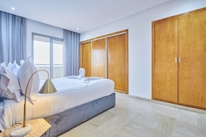 Ein Hotelzimmer mit Bett, Nachttischlampe, Kleiderschrank und einem großen Fenster.