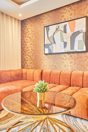 Ein modernes Wohnzimmer mit einem Ecksofa, einem Glastisch mit goldener Basis und einem an der Wand befestigten abstrakten Gemälde.