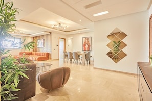A spacious living area with a sofa, dining table, and chairs, a decorative wall with geometric patterns, and a potted plant. - Designer 3BR in Prime Casablanca | Free Parking (Casablanca)