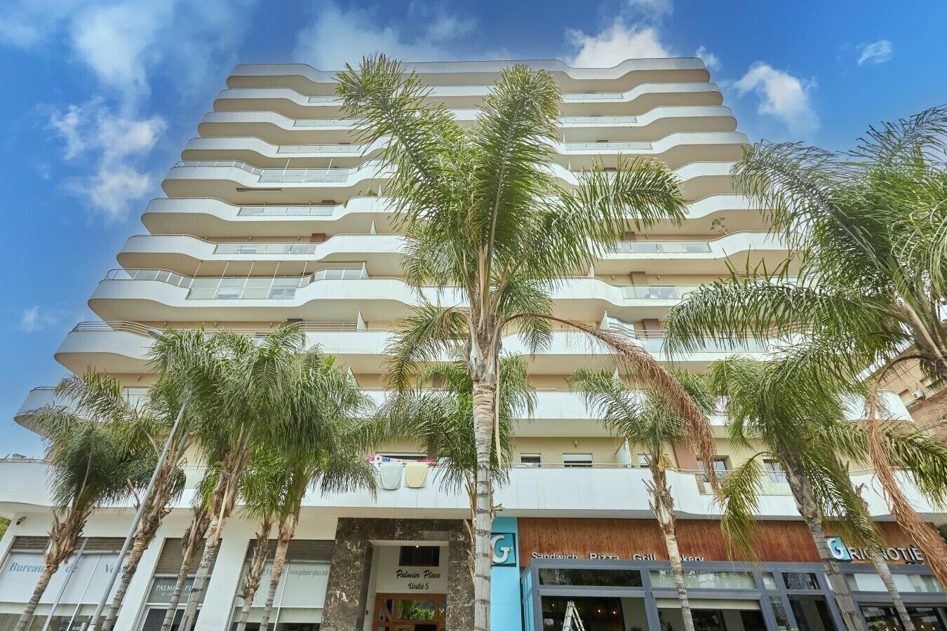 Ein mehrstöckiges Hotel im modernen Stil, mit Balkonen auf jeder Etage und einem markanten Eingang mit Beschilderung.
