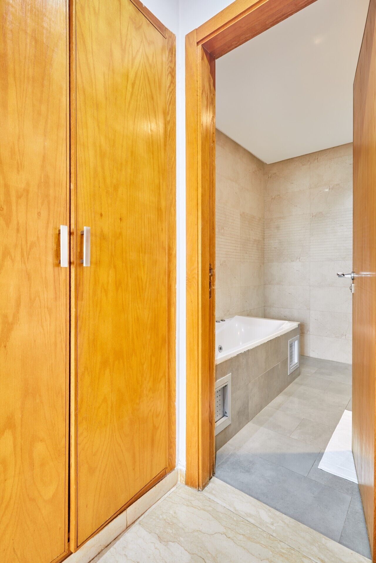 Ein Holzkleiderschrank mit Schiebetür, ein Badezimmer mit Badewanne und ein Fliesenboden.