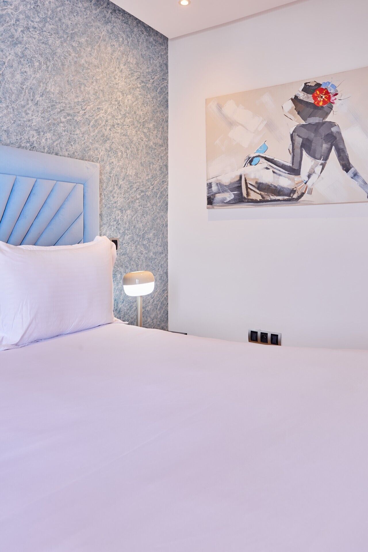Un dormitorio con una cama, una mesita de noche, una lámpara y un cuadro en la pared.