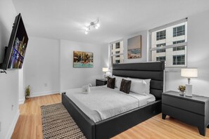 Ein modernes Schlafzimmer mit einem schwarzen Bett, weißen Wänden, einem Flachbildfernseher und Kunstwerken.