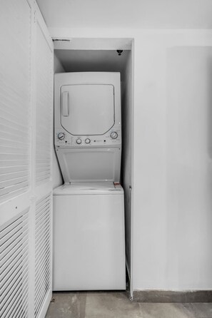 Een kleine wasruimte met een wasmachine en droger, een geventileerde muur en een betegelde vloer.