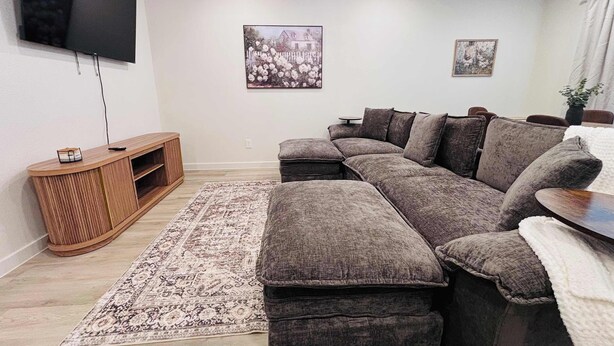 A living room with a sectional sofa, a flat-screen TV, a ceiling fan, and a decorative rug. - Colgate Cottage - 3BR/2BA - Family Friendly (Lubbock)