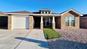 A residential house with a garage, a covered entryway, and a well-maintained lawn. - Colgate Cottage - 3BR/2BA - Family Friendly (Lubbock)
