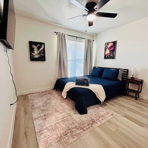 A bedroom with a bed, a ceiling fan, a window with curtains, and two wall-mounted paintings. - Colgate Cottage - 3BR/2BA - Family Friendly (Lubbock)