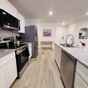 A modern kitchen with stainless steel appliances, a granite countertop, and a wooden dining table.