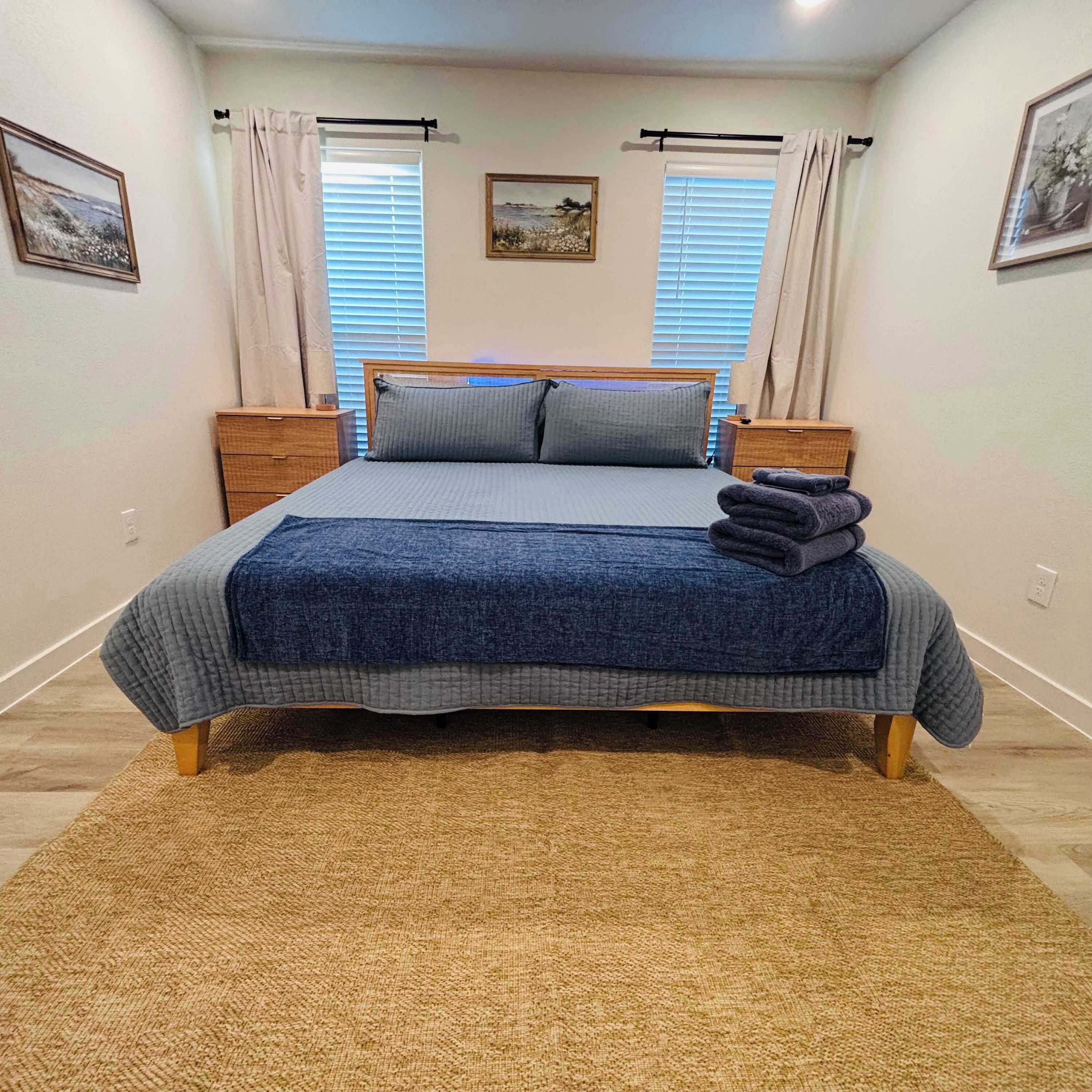 Une chambre à coucher avec un lit, deux tables de chevet, une fenêtre avec des rideaux et un tapis.
