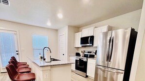 A modern kitchen with a central island, stainless steel appliances, and a seating area with bar stools. - Colgate Cottage - 3BR/2BA - Family Friendly (Lubbock)