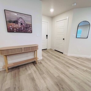 A hallway with a wooden bench, a framed picture on the wall, and a door with a mirror. - Colgate Cottage - 3BR/2BA - Family Friendly (Lubbock)