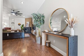 Ein modernes Wohnzimmer mit Kamin, einem großen Spiegel und einem Deckenventilator.