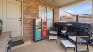 Un patio couvert avec un mur en briques, une porte, un distributeur automatique, un barbecue et des sièges d’extérieur.