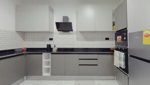Eine moderne Küche mit weißen Fliesenwänden, grauen Schränken, einer schwarzen Arbeitsplatte und einem Edelstahlbackofen.