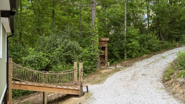 A gravel path leading to a wooden bridge over a stream, surrounded by dense forest.