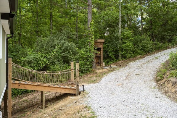 A gravel path leading to a wooden bridge over a stream, surrounded by dense forest.