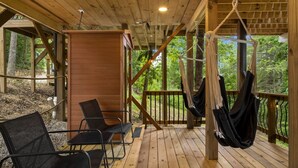 A wooden deck with a hammock, chairs, and a wooden wall.