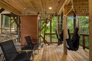 A wooden deck with a hammock, chairs, and a wooden wall.
