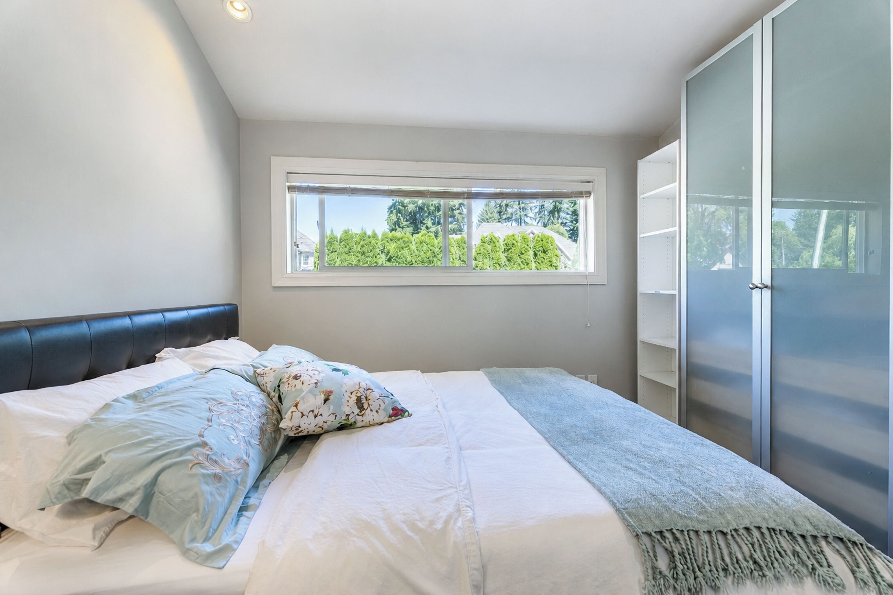 Een slaapkamer met een bed, een raam, een kledingkast en uitzicht op groen.