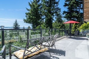 Un espace extérieur aménagé avec des chaises en métal et un parasol rouge, offrant une vue sur une zone boisée et un plan d’eau.