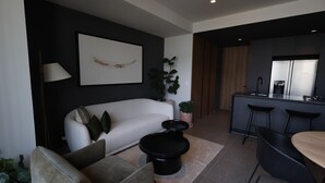 Una sala moderna con un sofá, una mesa de centro, un comedor con sillas, una cocina con un refrigerador y una planta en maceta.